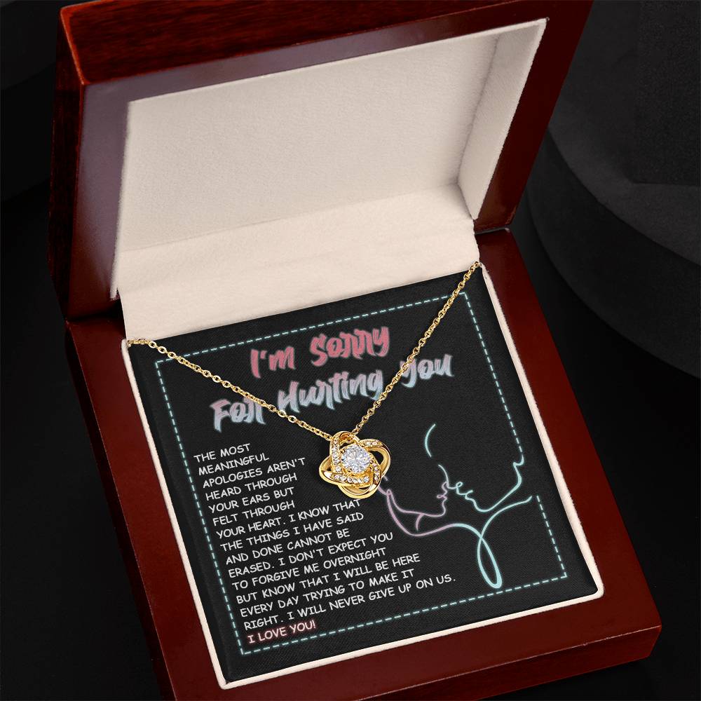 A 14k white gold Sorry-Never Give Up - Love Knot Necklace with an interlocked pendant set with cubic zirconia crystals sits on a note that reads, "I'm sorry for hurting you," accompanied by an apology message expressing regret, commitment to make things right, and affirming love.