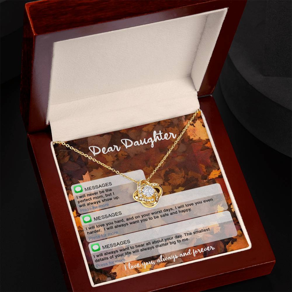 A gold necklace with a heart-shaped pendant in an open box. The yellow gold finish of the Daughter-Perfect Mom - Love Knot Necklace gleams, adorned with cubic zirconia crystals. The box insert reads "Dear Daughter" with text message-like affirmations about love and support printed beneath.