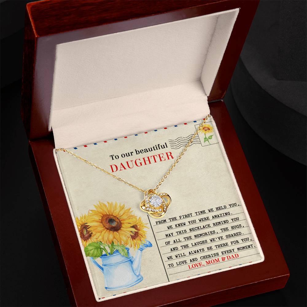 A Daughter-The First Time Love Knot Necklace featuring a heart and sunflower pendant in a wooden box. This personalized gift includes a card that reads "To our beautiful daughter" with a heartfelt message from Mom and Dad, making it an unforgettable token of love.
