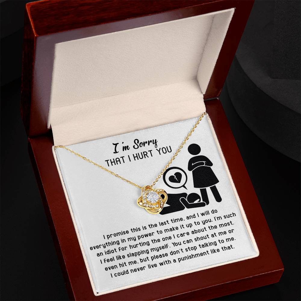 The Sorry-Stop Talking - Love Knot Necklace, embellished with cubic zirconia crystals, is elegantly presented in a wooden box. The box features a heartfelt message saying "I'm Sorry That I Hurt You," alongside an illustration of a woman and a heart symbol.