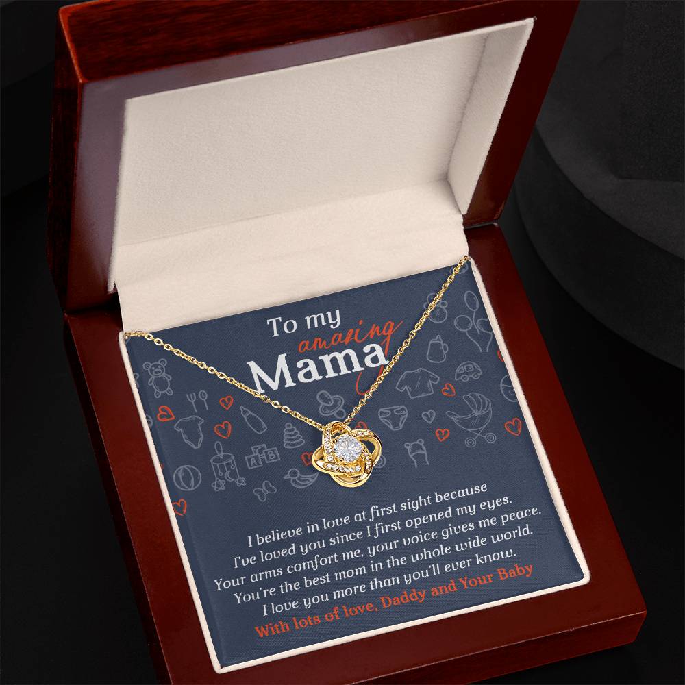 The Mom To Be-At First Sight Love Knot necklace, adorned with cubic zirconia crystals, is elegantly presented in an open red jewelry box. Inside the box is a heartfelt message to "Mama," conveying love and appreciation from "Daddy and Your Baby.