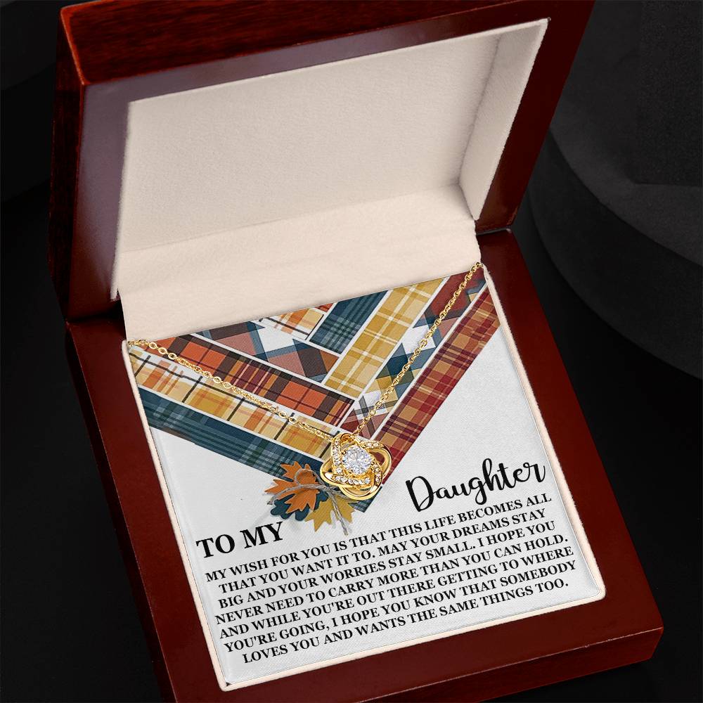 The "Daughter-The Same Things - Love Knot Necklace" with a heart pendant featuring leaves is displayed on a plaid-patterned card with an engraved message, inside an open wooden box. The pendant, crafted from 14k white gold and adorned with premium cubic zirconia crystals, adds a touch of elegance to the heartfelt presentation.