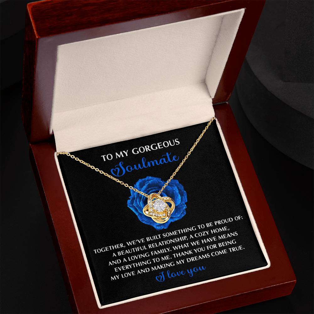 The Soulmate-Dreams Come True Love Knot Necklace in white gold features shimmering cubic zirconia and rests in a box with a touching message and blue rose graphic, symbolizing eternal love and connection.