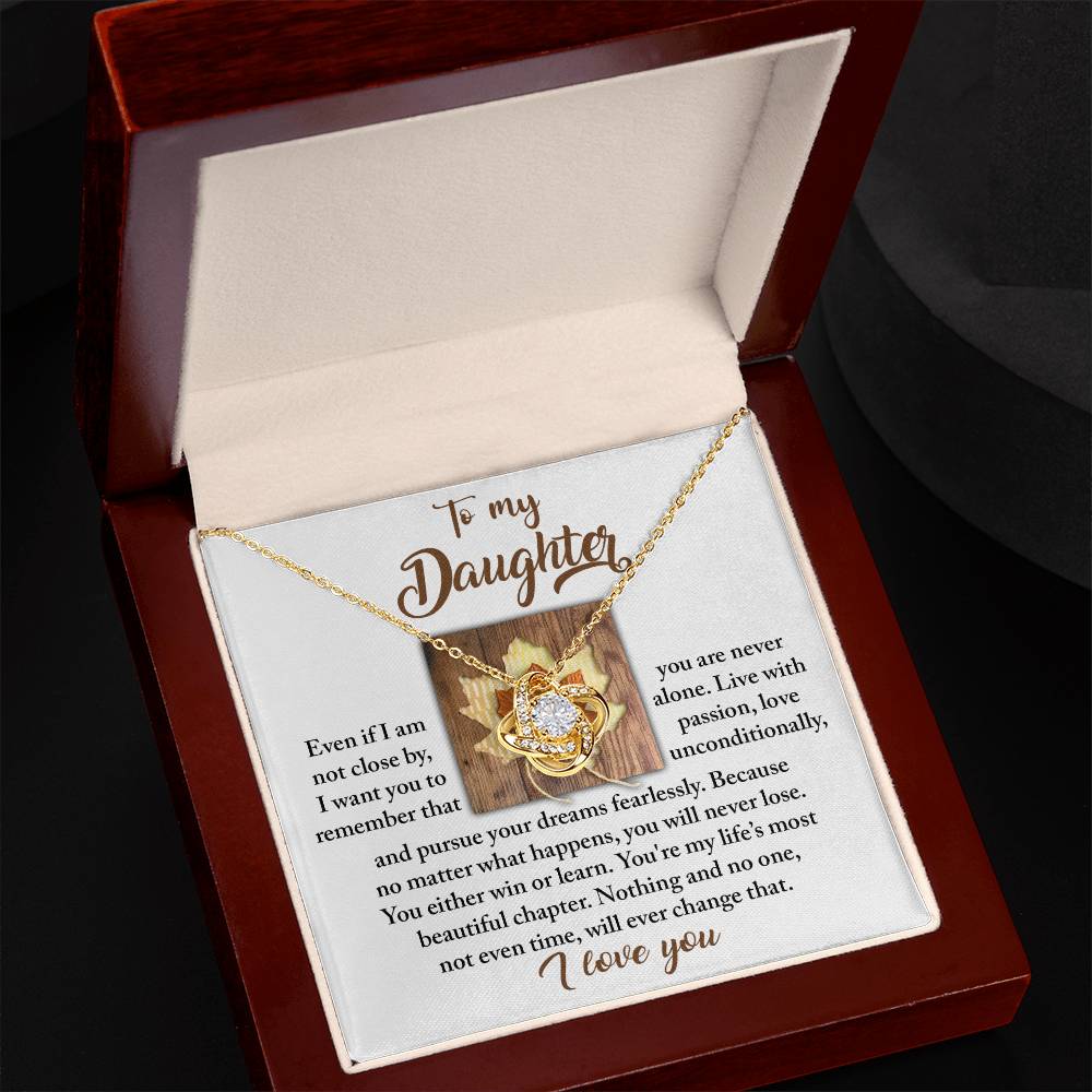 The Daughter-Live With Passion Love Knot Necklace, featuring an intertwined heart pendant crafted in 14k white gold and adorned with premium cubic zirconia crystals, rests in an open wooden box displaying a heartfelt message to a daughter.