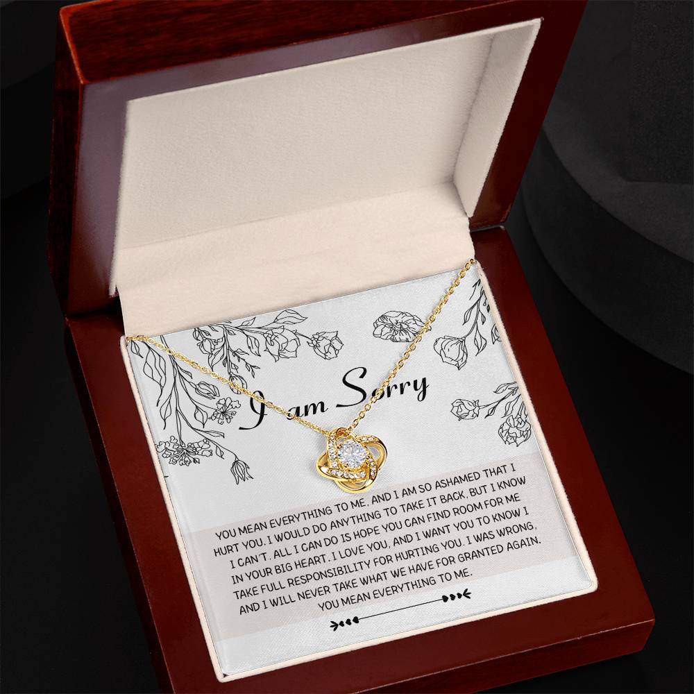 A Sorry-Your Big Heart - Love Knot Necklace with intertwined heart pendants rests in an open, cushioned box. The inside lid of the box features a printed apology message with floral illustrations and "I am Sorry" at the top, making it a heartfelt personalized gift adorned with premium cubic zirconia crystals.