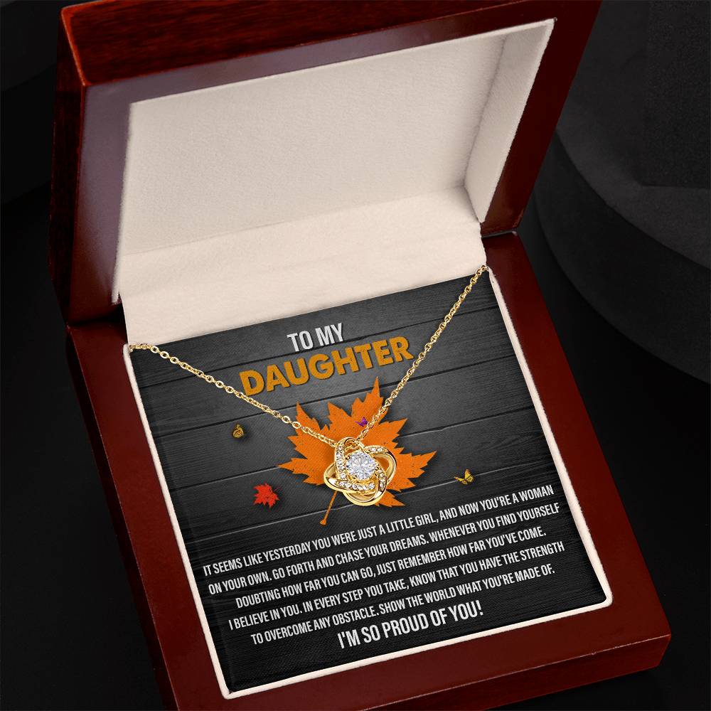 Introducing the "Daughter-You Can Go - Love Knot Necklace," a stunning gold piece nestled in a jewelry box adorned with cubic zirconia crystals. This necklace is accompanied by a heartfelt message specifically for a daughter and features a beautiful leaf design as the background.