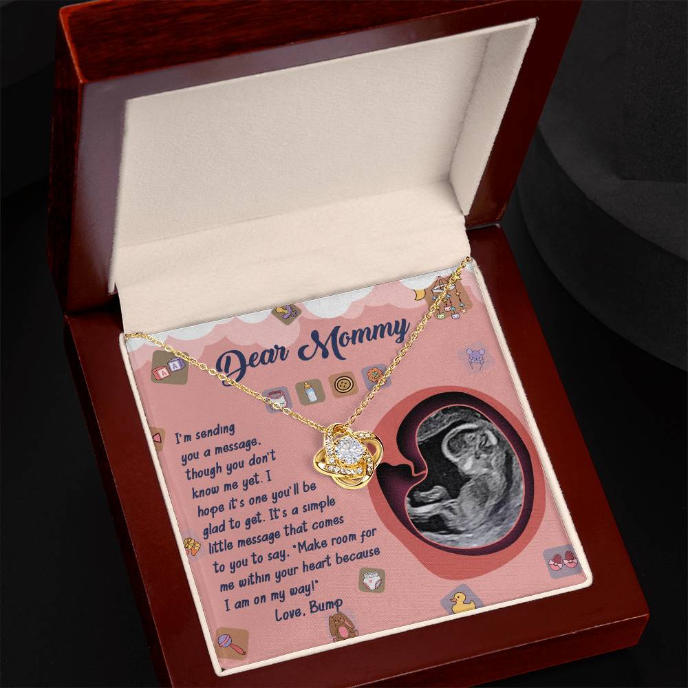 The "To Mom To Be, On My Way - Love Knot Necklace" with a heart-shaped pendant is showcased in an open jewelry box. Inside, there is a personalized message and an ultrasound image, making it the perfect personalized gift. Beautifully crafted, the pendant sparkles with exquisite cubic zirconia crystals.