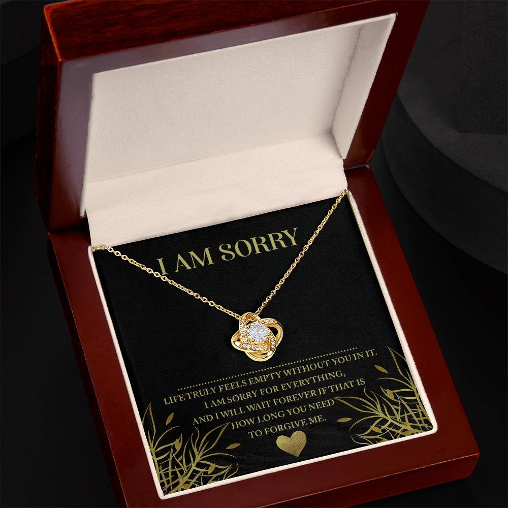 The Sorry-Without You Love Knot Necklace, featuring a heart-shaped pendant adorned with cubic zirconia crystals, is displayed in an open gift box. Inside the box is a heartfelt message that reads: "I AM SORRY. Life feels empty without you in it. I am sorry for everything..." This personalized gift speaks volumes.