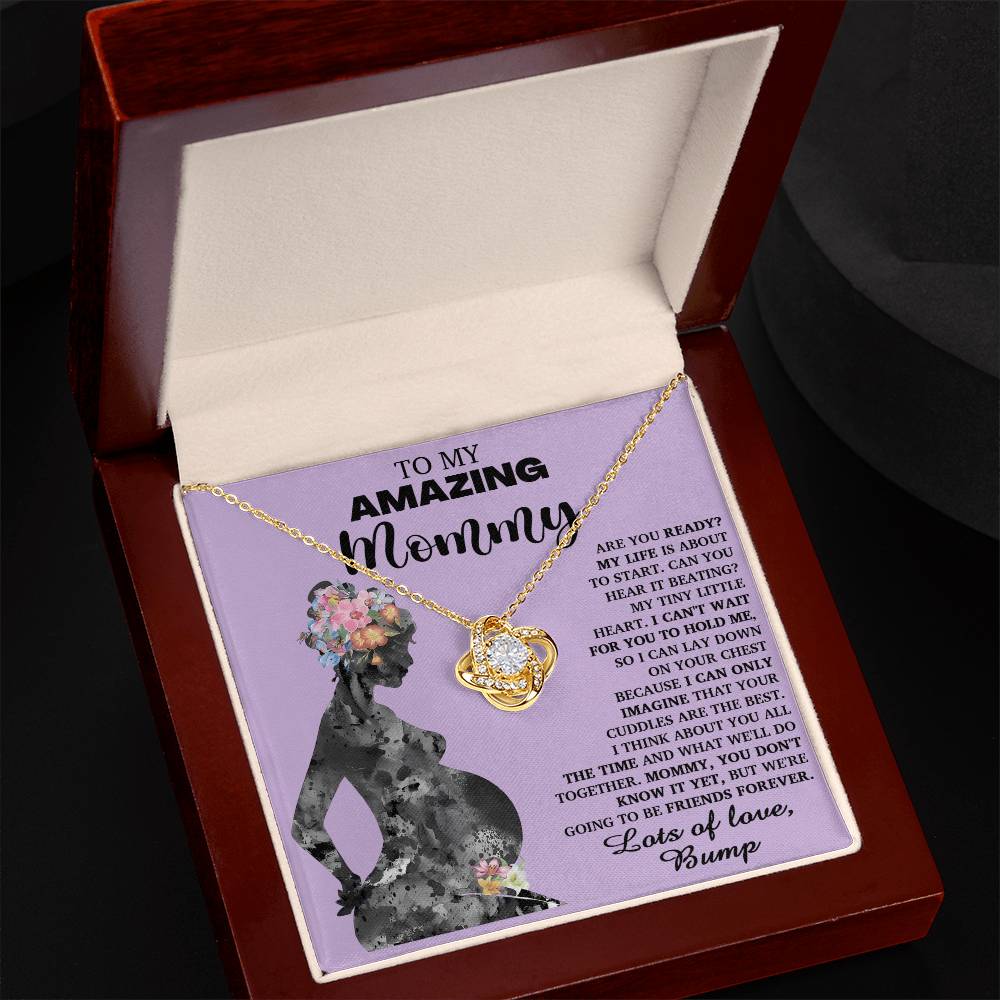 A "To Mom To Be, Tiny Little Heart - Love Knot Necklace" in a gift box with a card that reads "To My Amazing Mommy" and features a silhouette of a pregnant woman. The accompanying card includes a heartfelt message from the baby, signed "Bump." The intricate design represents the unbreakable bond between mother and child.