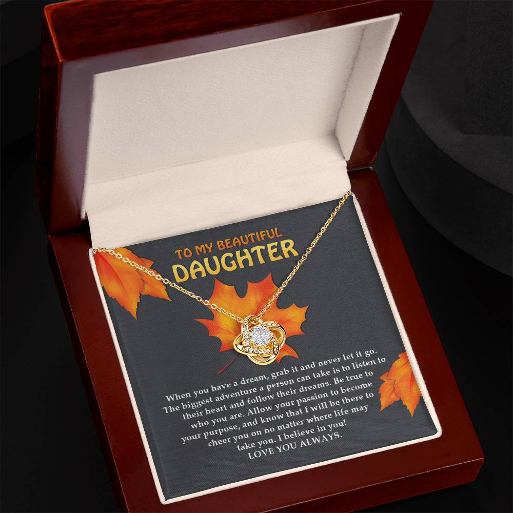 The Daughter-To Their Heart - Love Knot Necklace features a heart-shaped pendant adorned with premium cubic zirconia crystals, and is presented in a wooden jewelry box. The lid of the box showcases a heartfelt message, "TO MY BEAUTIFUL DAUGHTER," set against an autumn leaves background, making it the perfect personalized gift.