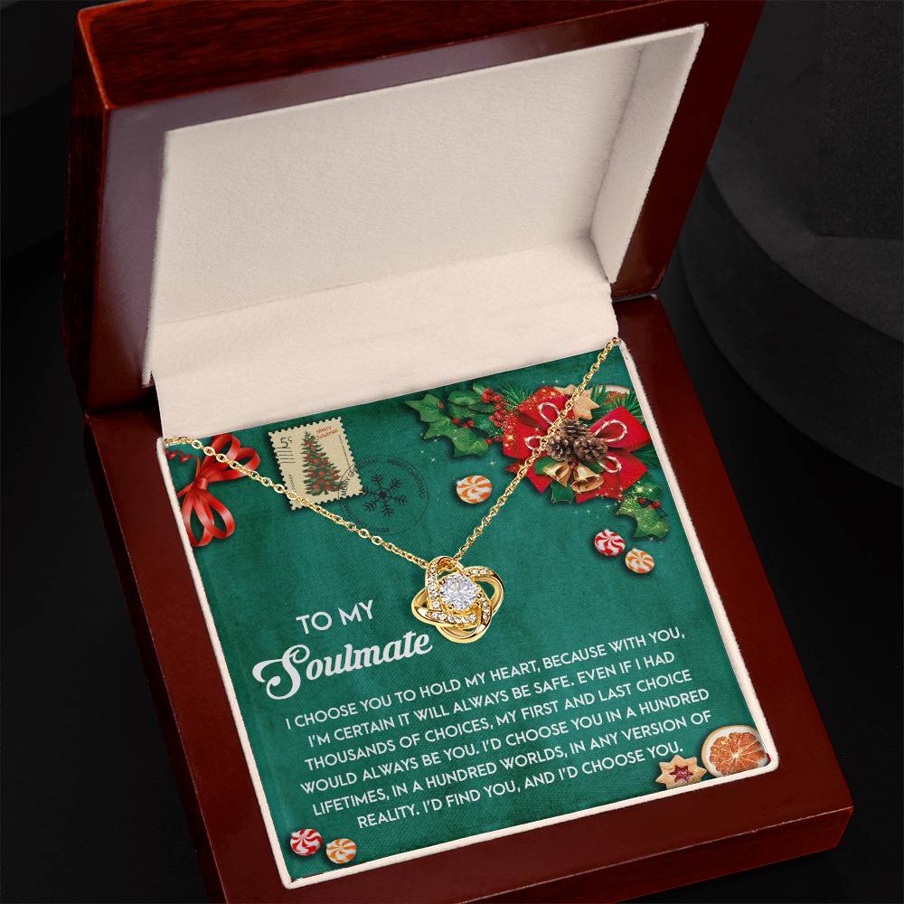 This Soulmate-Be Safe - Love Knot Necklace, featuring a heart-shaped pendant and adorned with cubic zirconia crystals, is presented in an open box. It includes a message card for your soulmate, complete with a festive design of holly and a Christmas tree.