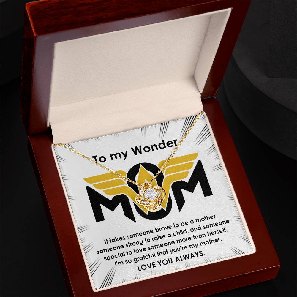 The "To Mom, More Than Herself - Love Knot Necklace" with a gold finish lies in a brown box, accompanied by a message card addressed "To my Wonderful Mom," expressing gratitude and admiration for her bravery and selflessness. Adorned with cubic zirconia crystals, it ends with "LOVE YOU ALWAYS.