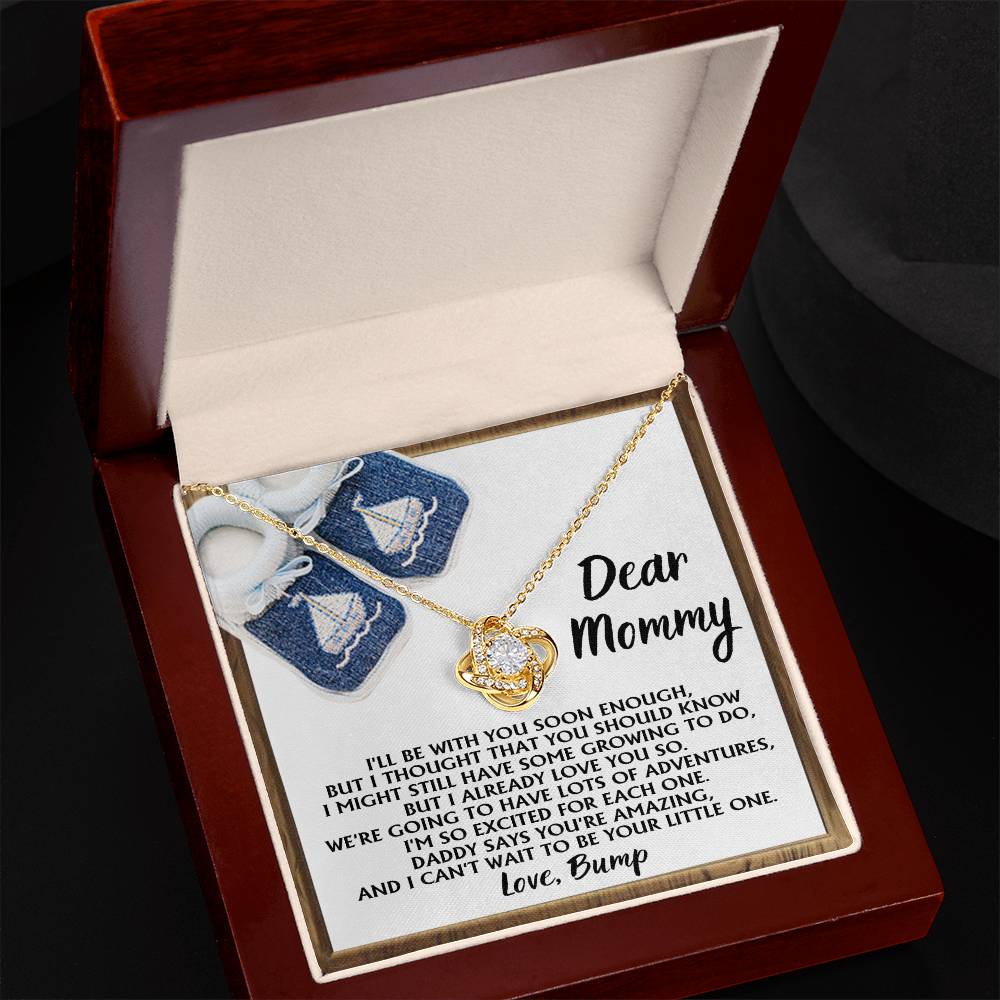 A jewelry box containing the "To Mom To Be, You're Amazing - Love Knot Necklace" in 14k white gold with a pendant and a heartfelt message from an unborn baby to "Mommy," expressing love and excitement about joining the family. The box also features small baby shoes, adding an extra layer of sentiment.