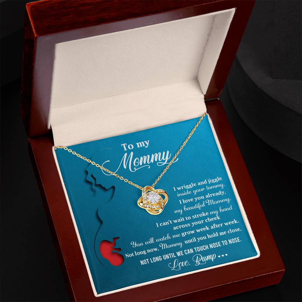 The "To Mom To Be, Nose To Nose - Love Knot Necklace" features an intertwined heart pendant adorned with sparkling cubic zirconia crystals and arrives in a jewelry box with a heartfelt message addressed to "Mommy" from an unborn baby, expressing love and anticipation for their future together.