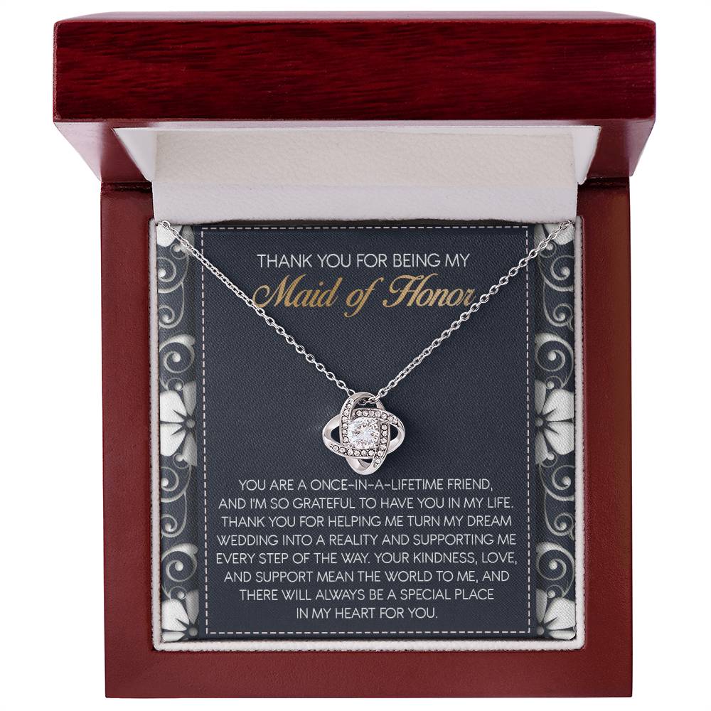The "To Maid of Honor, World To Me - Love Knot Necklace" features a heart-shaped pendant adorned with Cubic Zirconia Crystals. It comes beautifully packaged in a box that includes an inscribed thank-you note, expressing heartfelt gratitude to the Maid of Honor, making it a perfect personalized gift.