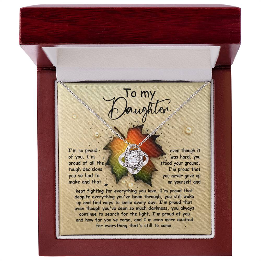 The Daughter-Stood Your Ground - Love Knot Necklace, featuring a heart pendant adorned with cubic zirconia crystals, is showcased in an open box. The lid of the box includes a heartfelt message titled "To my Daughter," conveying pride, love, and encouragement. The necklace is finished in stunning white gold, adding an elegant touch.