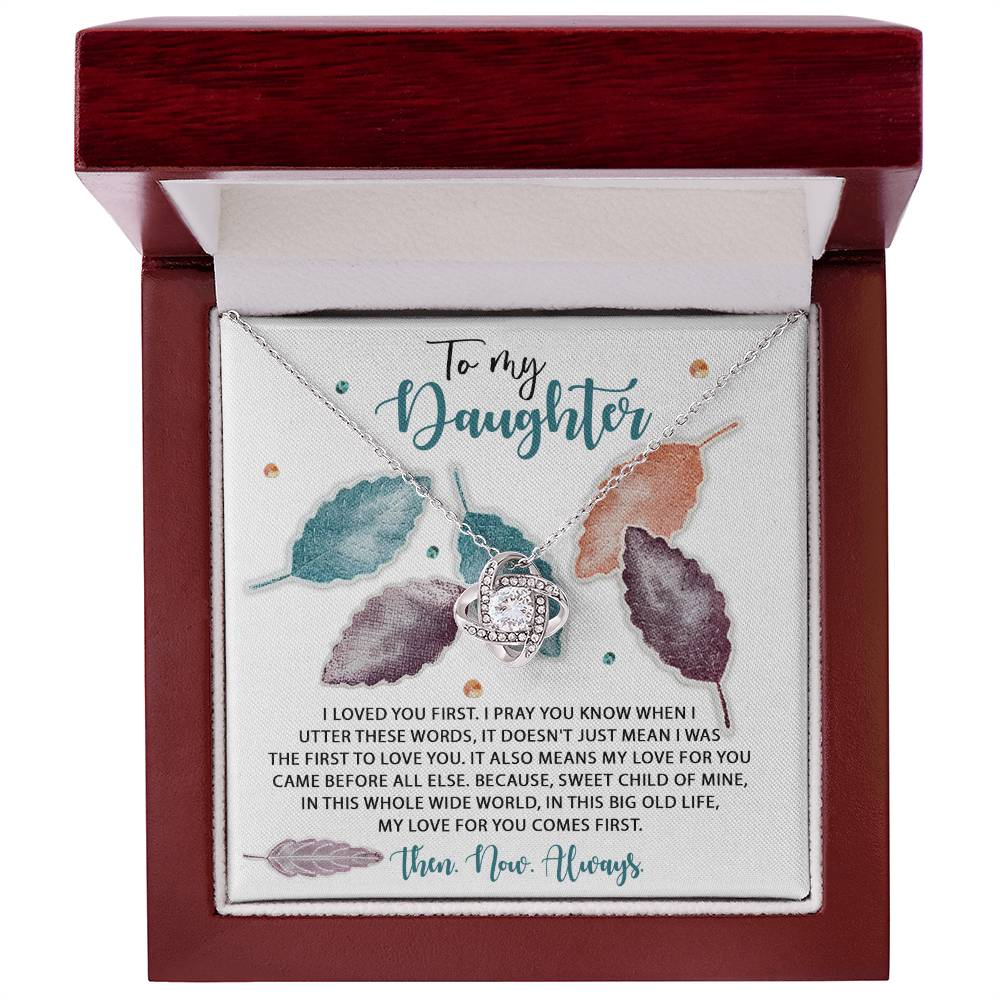 The Daughter-Pray You Know - Love Knot Necklace, featuring an interlocking heart design, is elegantly displayed inside a jewelry box. The box liner includes a heartfelt message for a daughter, complemented by a multicolored leaf design in the background. This personalized gift gleams with cubic zirconia crystals, adding an extra touch of elegance.