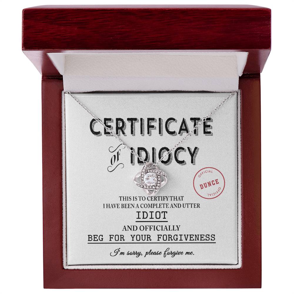 A red box contains the Sorry-Certificate Of Idiocy - Love Knot Necklace adorned with cubic zirconia crystals and an apology card titled "Certificate of Idiocy," asking for forgiveness.