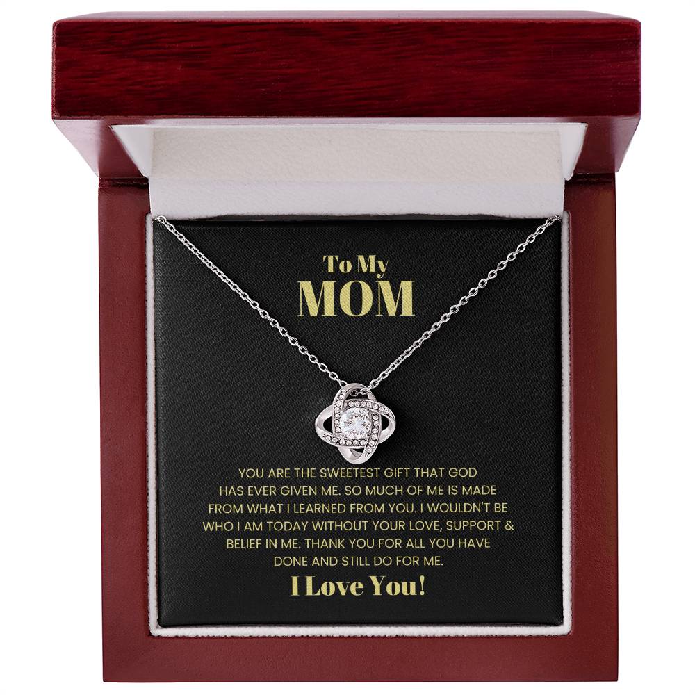 The "To My Mom, You Are The Sweetest Gift - Love Knot Necklace," featuring premium cubic zirconia crystals, delicately rests in a red box. The box's interior has a printed message expressing love and gratitude to a mother, making it a perfect personalized gift.