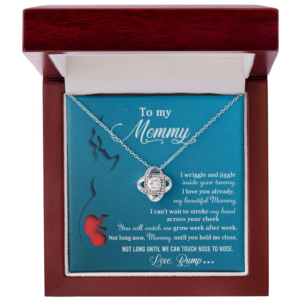 A "To Mom To Be, Nose To Nose - Love Knot Necklace" crafted in 14k white gold, adorned with sparkling cubic zirconia crystals, rests elegantly in a wooden box against a teal background. Inside the lid is a heartfelt message addressed to "Mommy.