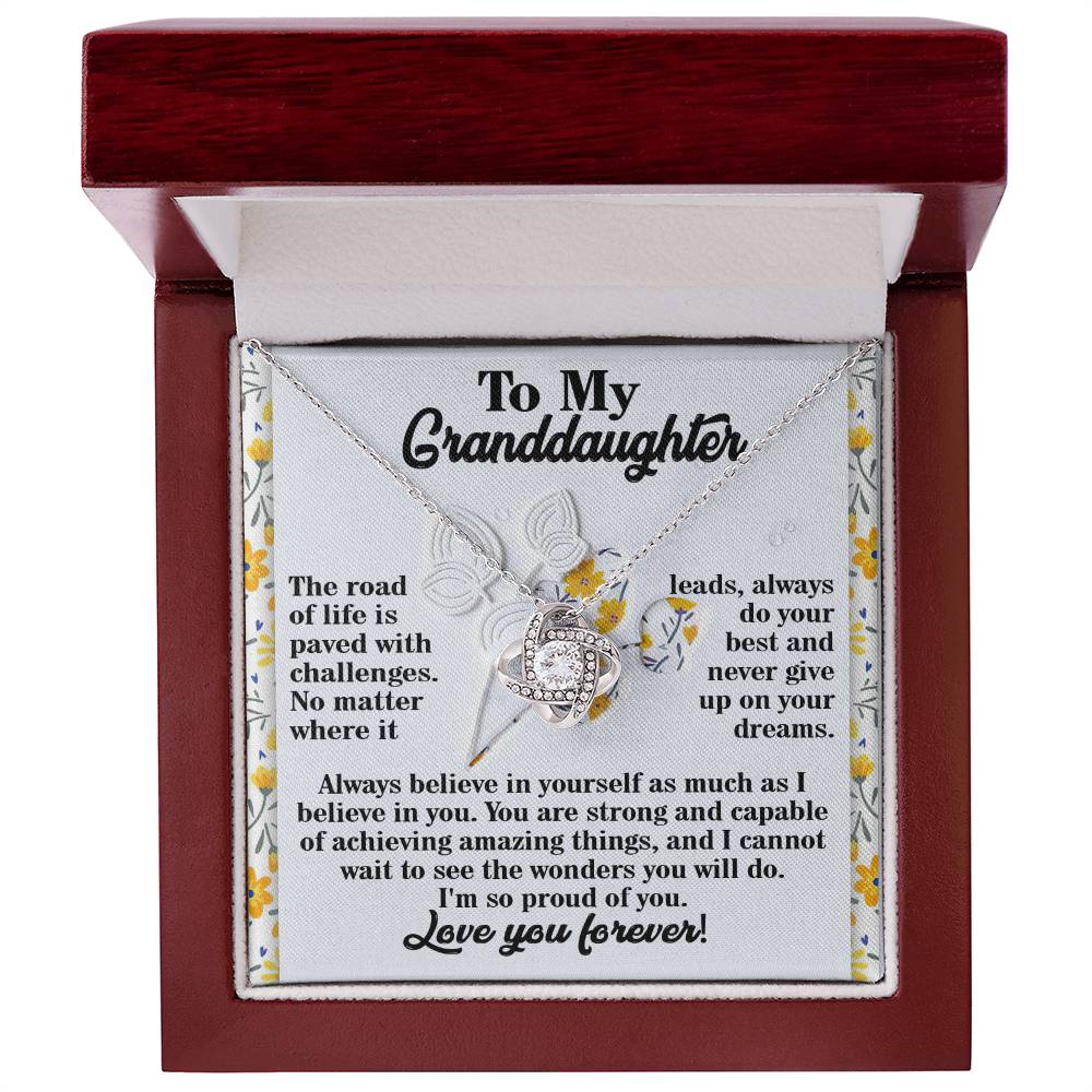 The Granddaughter-On Your Dreams - Love Knot Necklace, crafted from 14k white gold and adorned with radiant cubic zirconia crystals, is elegantly displayed in an open jewelry box, conveying a heartfelt message to a granddaughter to believe in herself and follow her dreams.