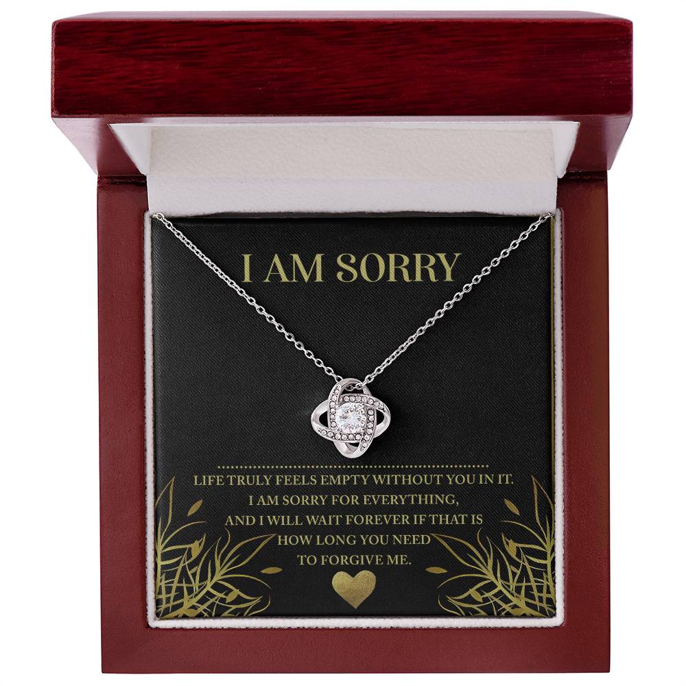 The "Sorry-Without You - Love Knot Necklace," featuring a silver heart pendant embellished with cubic zirconia crystals, is elegantly presented in a red box. The lid of the box showcases an apology message with the words "I AM SORRY" in large gold letters, making it a beautifully personalized gift.