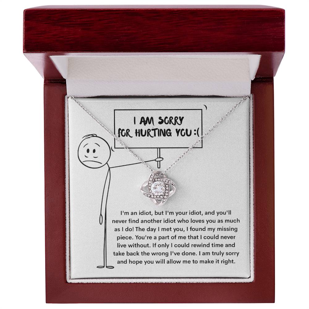 The Sorry-Missing Piece Love Knot Necklace, adorned with cubic zirconia crystals, features a pendant displayed in an open wooden box. Inside the lid is an illustration of a stick figure holding a sign that reads "I am sorry for hurting you." Below it is a heartfelt apology message, making this classic gift a touching symbol of reconciliation.