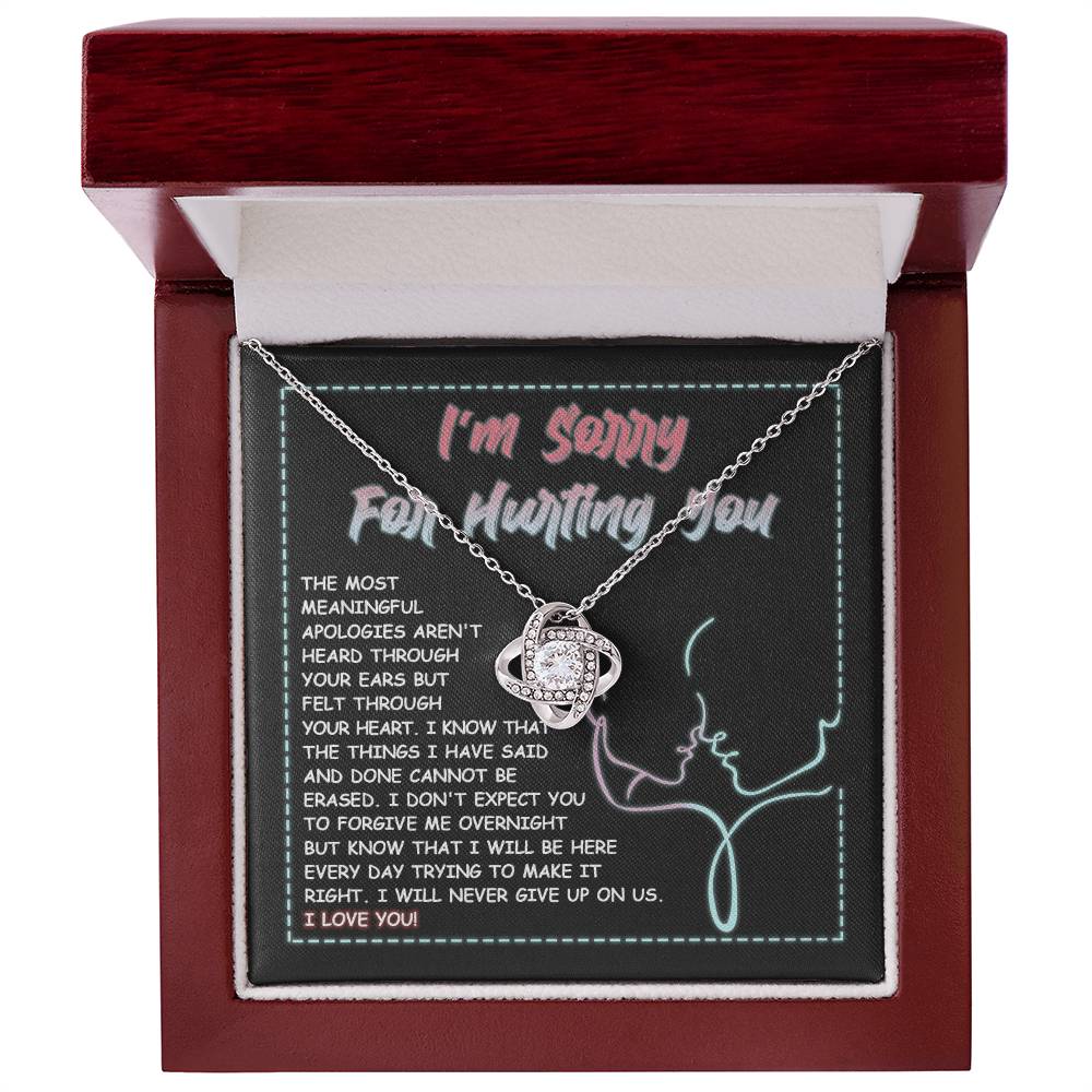 A 14k white gold Sorry-Never Give Up - Love Knot Necklace with an interlocked pendant set with cubic zirconia crystals sits on a note that reads, "I'm sorry for hurting you," accompanied by an apology message expressing regret, commitment to make things right, and affirming love.
