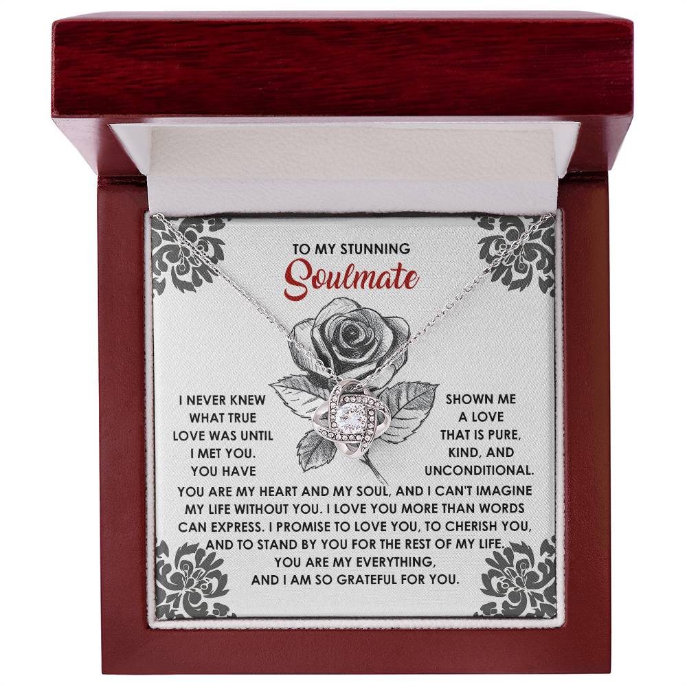 This personalized Soulmate-Cherish You necklace, featuring a Love Knot adorned with cubic zirconia crystals, is elegantly displayed in a wooden box. The inside lid reveals a heartfelt message to a "soulmate," beautifully framed by floral decorations.