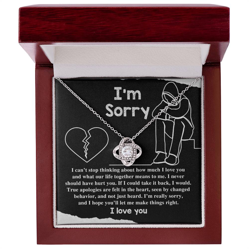 The "Sorry-Not Just Heard - Love Knot Necklace" features an apology message on a black background. The heartfelt text expresses regret and a promise to change, accompanied by illustrations of a heart and a person sitting with their head down. Cubic zirconia crystals add a touch of elegance, with "I love you" written at the bottom.