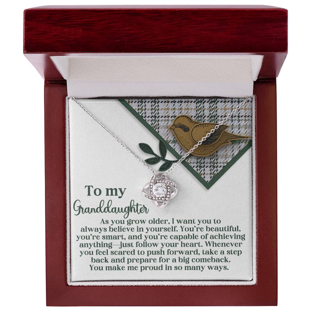 The Granddaughter-A Big Comeback - Love Knot Necklace, featuring a stunning gold finish and a sparkling cubic zirconia pendant, is elegantly presented in an open wooden box that includes a heartfelt message encouraging your granddaughter to embrace confidence and resilience.