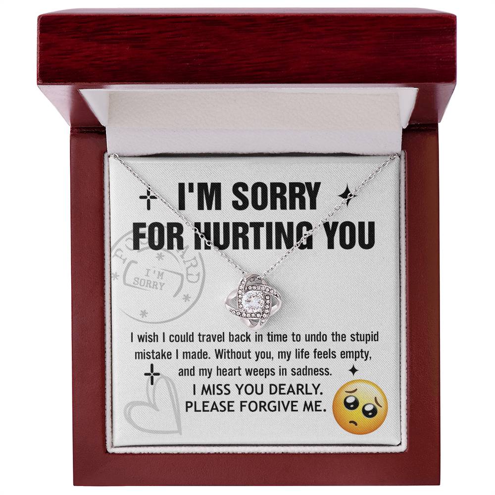 A Sorry-Travel Back - Love Knot Necklace with a white gold finish is displayed on a card featuring the text: "I'M SORRY FOR HURTING YOU," along with an apology note and a sad face emoji at the bottom right.