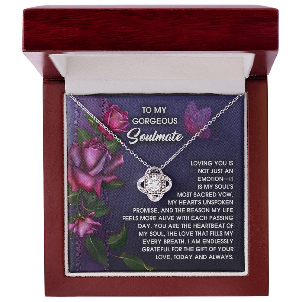 The Soulmate-Unspoken Promise - Love Knot Necklace, featuring cubic zirconia crystals and a planetary design in white or yellow gold, elegantly rests in an open wooden box. A romantic message for a soulmate is framed by delicate rose designs on the backdrop.
