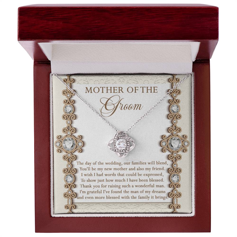 To Mom Of Groom, New Mother - Love Knot Necklace with an interlocking heart pendant, adorned with cubic zirconia crystals, on a card reading: “Mother of the Groom” and a heartfelt message appreciating the groom's mother. Available in white gold or yellow gold finish.