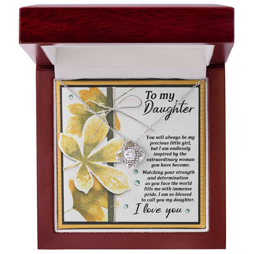 The Daughter-Blessed To Call - Love Knot Necklace with a cubic zirconia crystal pendant sits in an open red jewelry box. Behind it is a note that reads: "To my Daughter... Watching your strength and determination... I love you." The necklace features a stunning white gold finish.