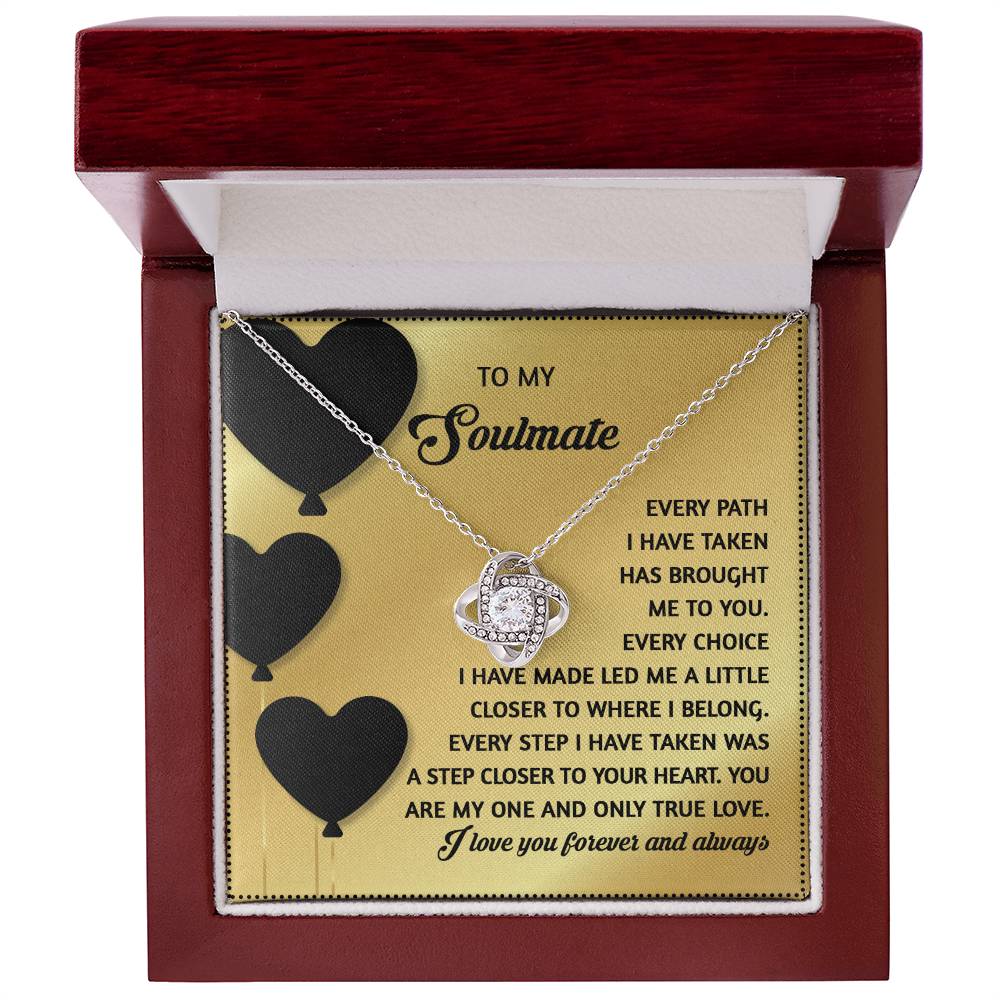 The Soulmate-A Step Closer - Love Knot Necklace features a cubic zirconia pendant and comes in a box with gold card showcasing black and gold text, enhanced by heart illustrations for elegance with its delicate gold finish.