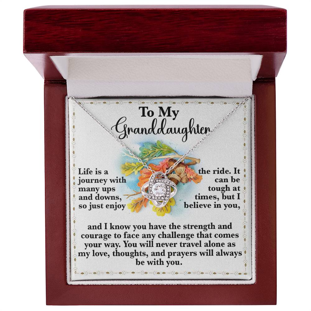 The Granddaughter-Never Travel Alone - Love Knot Necklace comes in a beautifully designed box with an inspiring message for a granddaughter. It features a delicate floral pattern and touching text about life's journey, belief, and support. Adorned with sparkling Cubic Zirconia, this necklace is the ideal gift for a loved one to cherish forever.