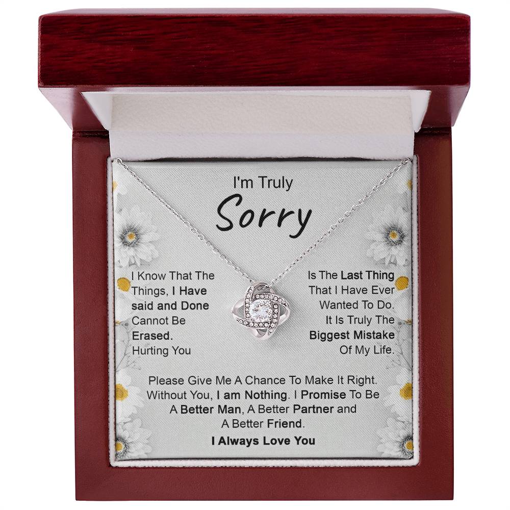 The "I’m Truly Sorry - Love Knot Necklace," featuring a pendant adorned with cubic zirconia crystals, rests on a heartfelt message that reads, "I'm Truly Sorry." The text conveys remorse for past actions and a commitment to becoming a better person, partner, and friend. The background is decorated with delicate floral designs.
