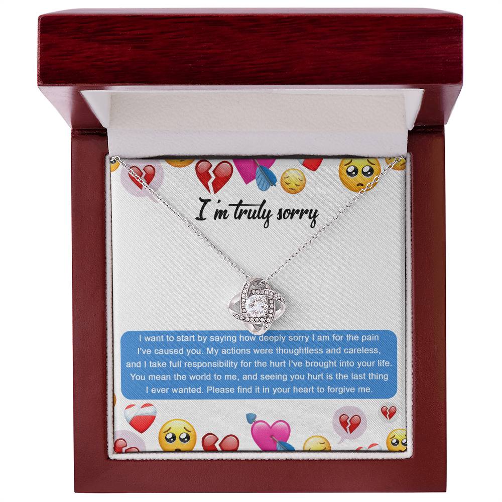 The Sorry-How Deeply Sorry - Love Knot Necklace features a pendant with an intertwined design, adorned with sparkling cubic zirconia crystals. The piece rests on a card that includes an apology message accompanied by various emoticons, such as hearts and sad faces.