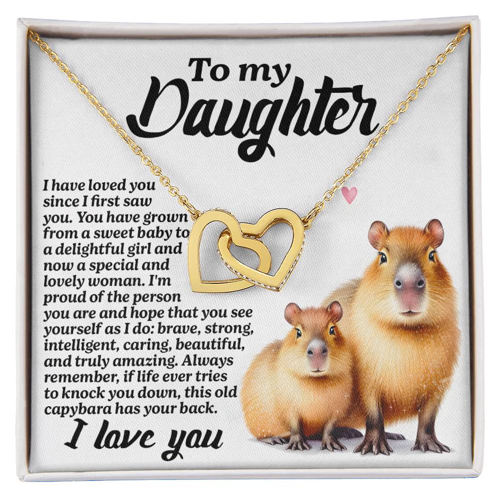 The Daughter-Sweet Baby Interlocking Hearts Necklace features a rose gold finish with cubic zirconia, presented on a card with capybaras, a pink heart, and a loving message from a parent to their daughter. The white background accentuates its elegance.