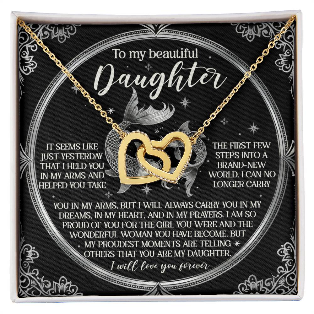 The Daughter-In My Prayers - Interlocking Hearts Necklace, in gold with cubic zirconia crystals, rests on a black card reading "To my beautiful daughter" along with a heartfelt message. A circular floral motif beautifully enhances the presentation.