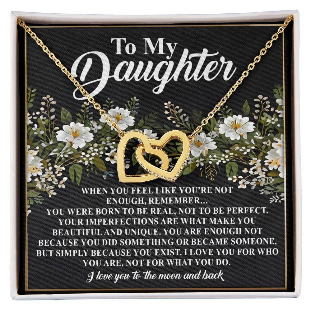 A rose gold Interlocking Hearts necklace, adorned with cubic zirconia crystals, rests on a black card with white floral designs. The card's message, "To My Daughter," speaks of self-worth and love, ending with "I love you to the moon and back." Product: Daughter-What You Do Necklace.