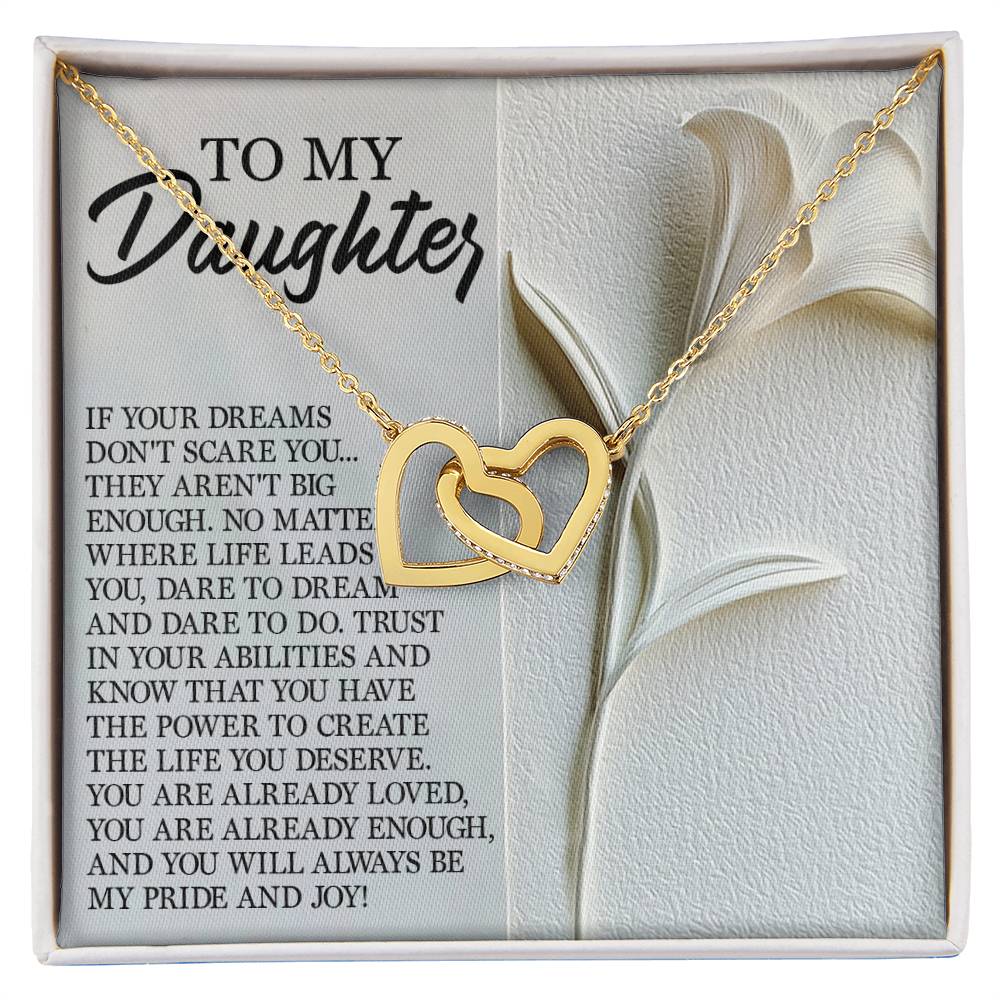 The Daughter-Dare Dream - Interlocking Hearts Necklace, crafted in surgical steel with a rose gold finish, rests on a "To My Daughter" card showcasing an inspirational message about dreams, trust, and self-worth. Sparkling cubic zirconia crystals and a white lily design enhance the stunning display.