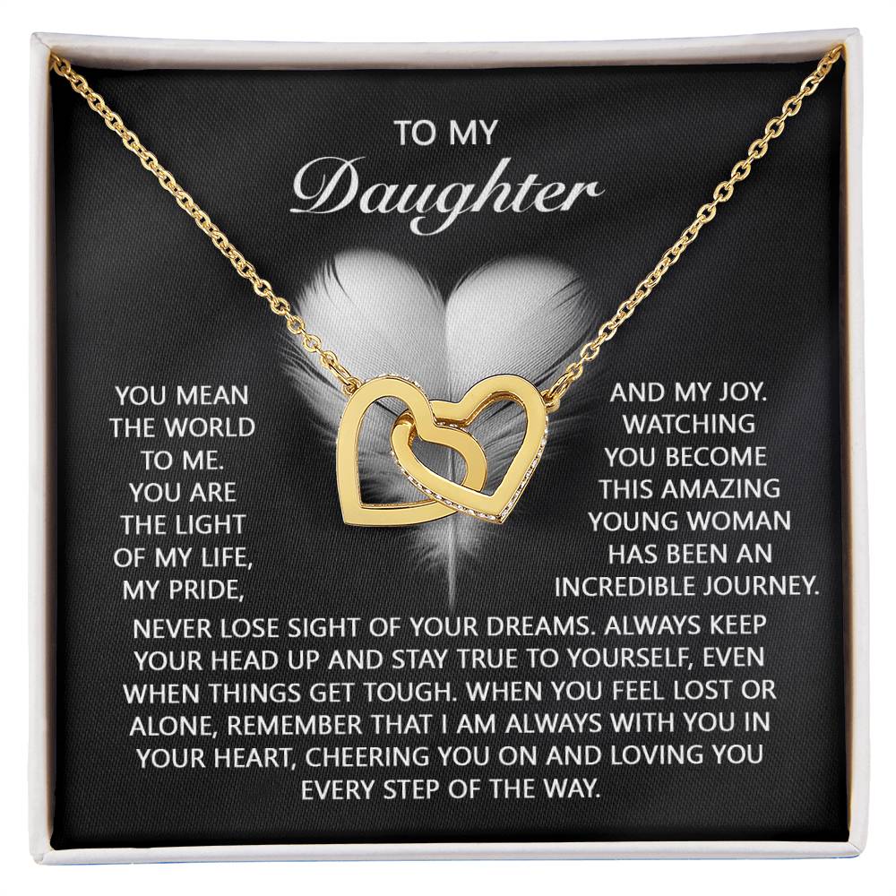 The "Daughter-In Your Heart - Interlocking Hearts Necklace" features surgical steel with a rose gold finish, adorned with cubic zirconia crystals. It rests on a black card displaying a heartfelt message for your daughter, complete with a delicate feather graphic in the background.
