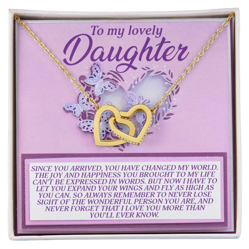 The Daughter-Expand Wings Interlocking Hearts Necklace features gold hearts adorned with cubic zirconia crystals on a purple card inscribed with "To my lovely Daughter," surrounded by floral and heart designs, conveying a heartfelt message of love, joy, and remembrance.
