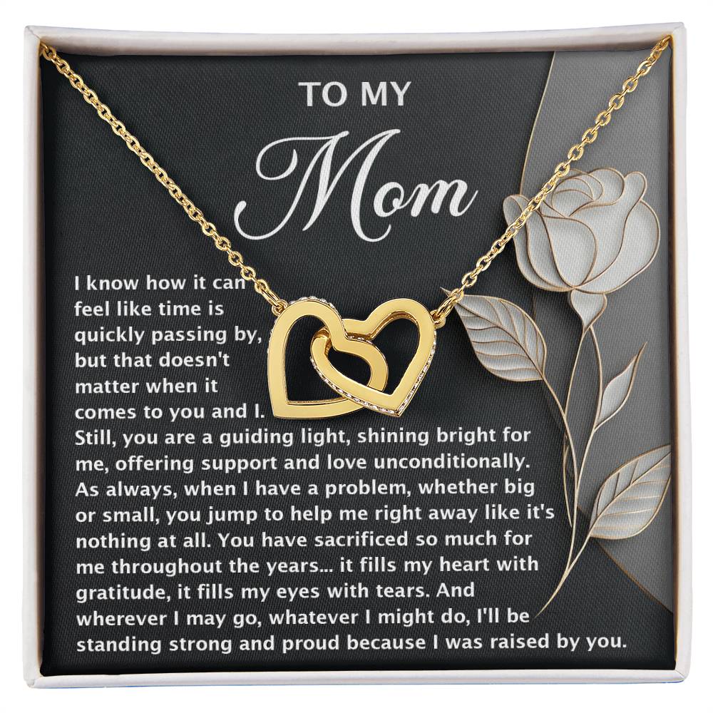 The Mom-Guiding Light Interlocking Hearts Necklace in gold, adorned with cubic zirconia crystals, features a rose-accented card with a heartfelt message of gratitude and love for a mother's support and sacrifices. It's the perfect gift for her.