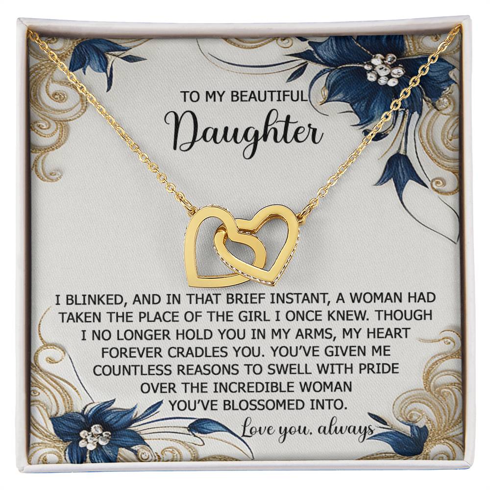 A stunning "Daughter-In My Arms" Interlocking Hearts Necklace, adorned with cubic zirconia crystals, is presented on a floral-decorated card that reads, "To my beautiful daughter," carrying a heartfelt message.