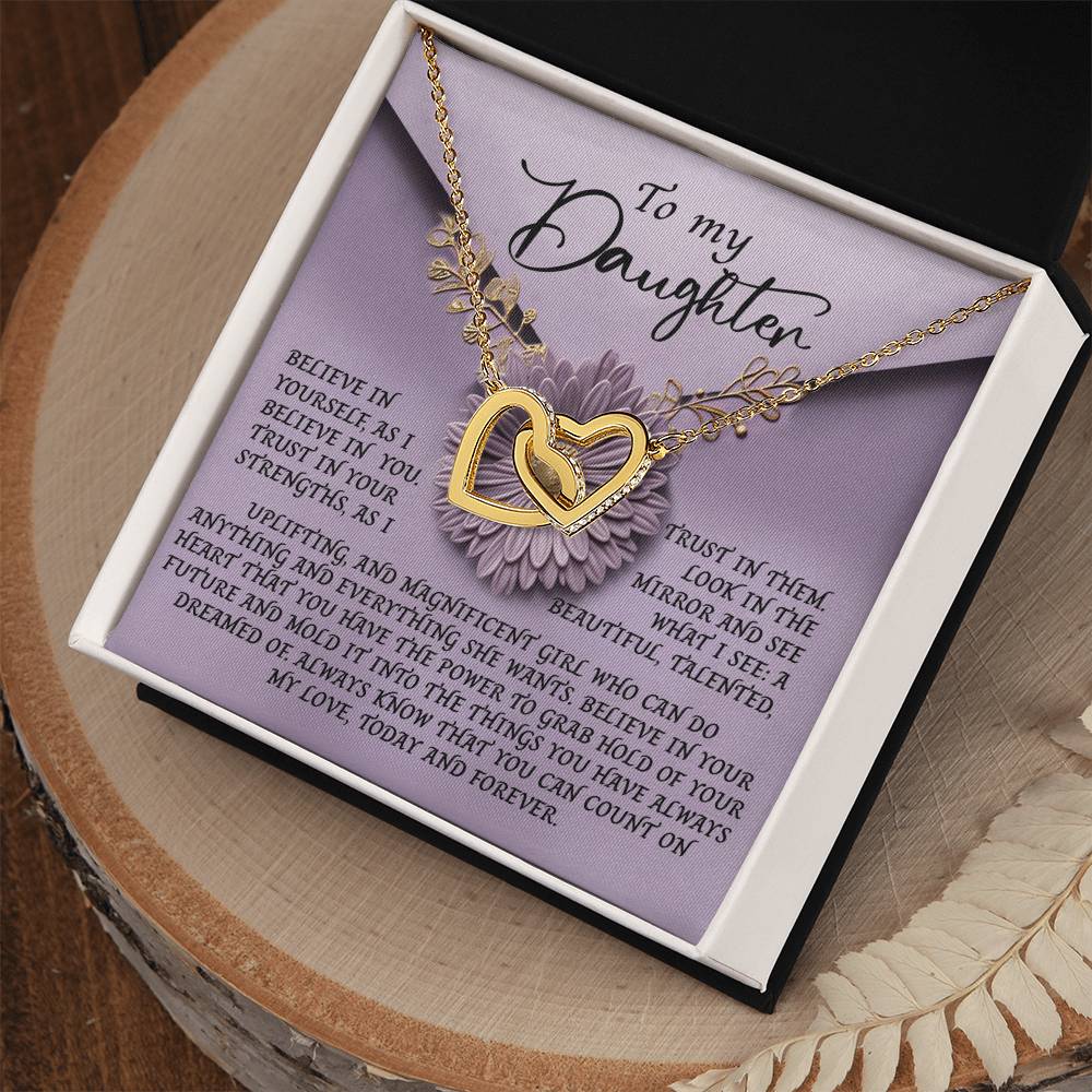 A gift box containing the "Daughter-Magnificent Girl - Interlocking Hearts Necklace" features a rose gold finish with cubic zirconia crystals set against a purple flower background. The card says "To my Daughter," offering a heartfelt message of self-belief, love, and pride.