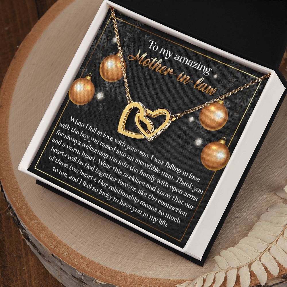 The Mother-in-Law-Two Hearts Interlocking Hearts Necklace, featuring a rose gold finish and adorned with sparkling cubic zirconia crystals, is elegantly displayed on a card bearing a heartfelt message for your mother-in-law, all beautifully presented in an open gift box.