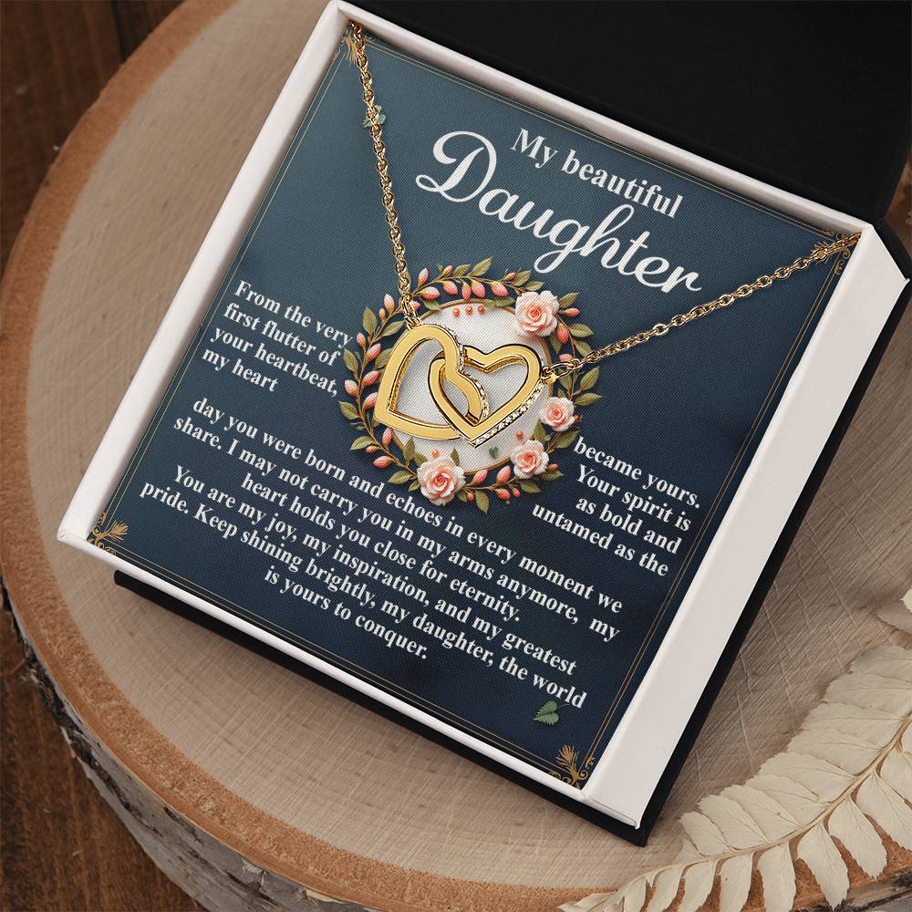 The Daughter-First Flutter Interlocking Hearts Necklace in rose gold lies in an open box, surrounded by pink roses and greenery. The inner lid features a heartfelt message under the title "My Beautiful Daughter.